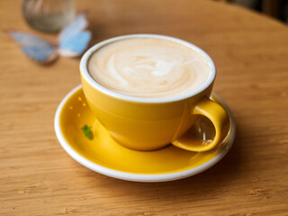 Yellow coffee cup with a white saucer sits on a wooden table