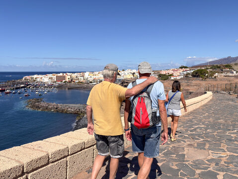 Rear view of two men and one senior woman on outdoor hike along the sea enjoying sunny day in good company. Healthy and leisure activity in retirement. Horizon over water - Powered by Adobe