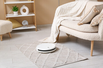 Modern robot vacuum cleaner on carpet near sofa at home
