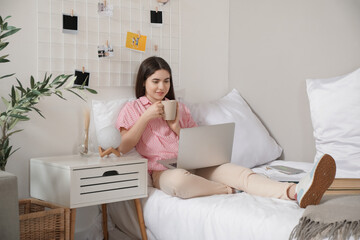 Female student with cup of tea and laptop studying on bed at home