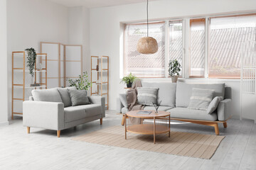 Interior of living room with grey sofas, coffee table, houseplants and folding screen near white wall
