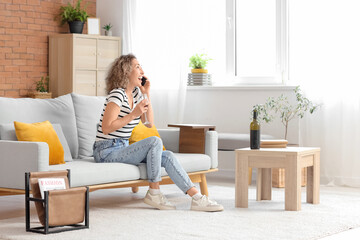 Happy middle-aged woman with glass of red wine talking by phone at home