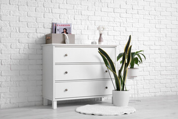 Chest of drawers with houseplants and decor near white brick wall