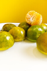 Peeled oranges placed on top of Tangerine oranges in water with yellow background. Tangerine orange texture in vertical. Healthy eating, fresh fruit, eating, vitamin, food, peel, and water concepts.