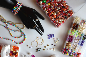 Fototapeta premium Hand figurine, colorful friendship bracelets, necklaces, various beads and DIY supplies on the table. Making jewelry at home. Flat lay.