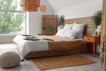 Large bed, bedside tables and pouf decorated with palm branches in bedroom