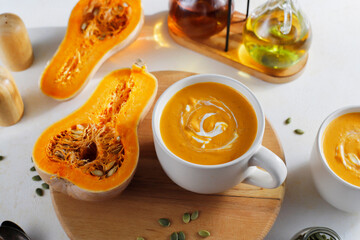 Roasted butternut squash soup with cream and pumpkin seeds on two white mugs.