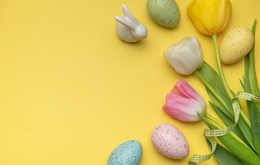 Easter eggs and tulips forming a frame on a yellow background