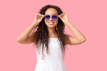 Beautiful African-American woman with sunglasses on pink background