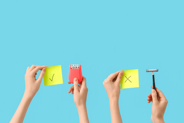 Female hands with razor, modern epilator and sticky notes on blue background