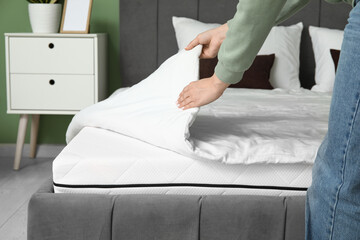 Woman with soft orthopedic mattress making bed at home, closeup