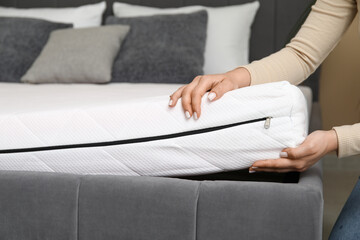 Woman putting soft orthopedic mattress on bed at home, closeup