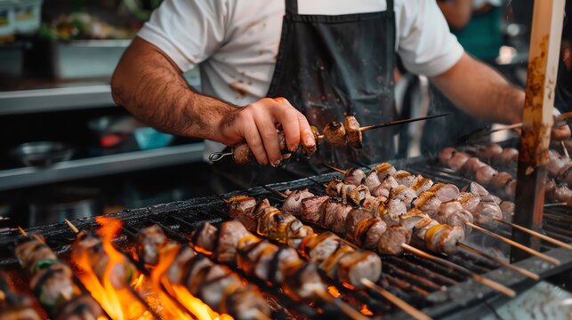 A chef is grilling skewers of meat and vegetables over an open flame. The chef is wearing a white shirt and black apron.