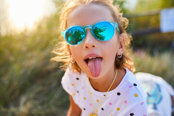 Young girl enjoys sunny day outdoors with playful expression and bright sunglasses