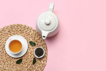 Cup and teapot of hot tea with dried leaves on pink background
