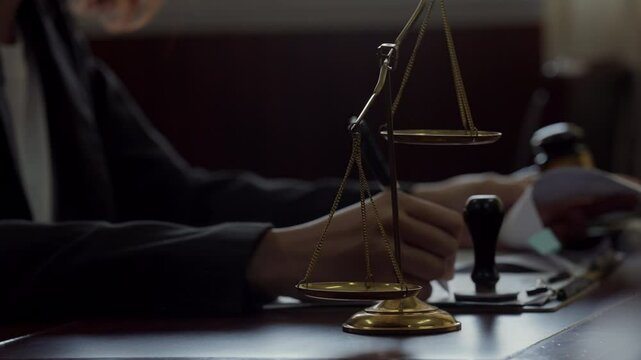 A person is sitting at a desk with a scale and a pen. The scale is gold and has a black tip. The person is likely a lawyer or a judge, as they are holding a pen and a piece of paper