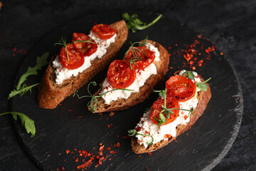 Board of tasty tomato bruschetta with ricotta on black background