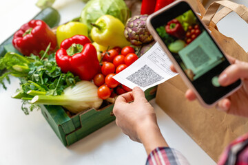 Female person scanning qr code of receipt using smart phone on background of box with vegetables