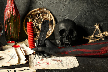 Bloody witch hand with magic attributes writing spell on grunge black background. Halloween...