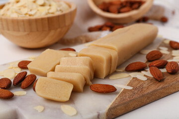 Cutting board with tasty marzipan, almond nuts and flakes on light table, closeup