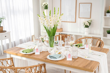 Stylish table setting with vase of Gladiolus flowers and candles near window in kitchen