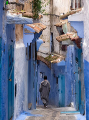 Man in  traditional jlaba robe walks away from camera in the blue and white painted old town Medina...