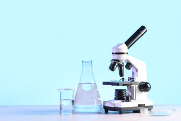 Modern microscope and laboratory glassware with liquid on white table
