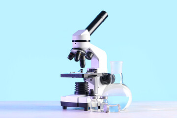 Modern microscope, ampules and laboratory flask with liquid on white table
