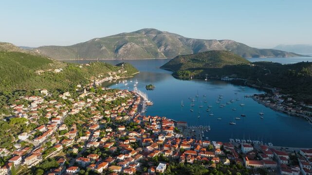 Sunrise over Vathy, Ithaca, Greece, with soft golden light reflecting on the calm bay waters, panoramic aerial tilt down