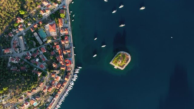 Aerial top down orbit of Lazareto Island in Vathy, Ithaca, Greece, with boats moored around the historic landmark, textured city along the coast