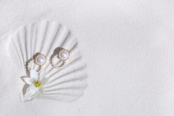 Stylish earrings and beautiful flower on white sand