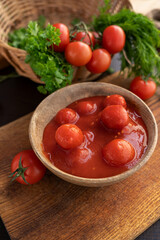 Cherry tomatoes, tomato paste in its own juice in a wooden plate on a wooden board background. Natural tomato paste with whole tomatoes. Preparation of sauces and food.