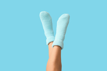 Legs of young woman in warm blue socks on color background