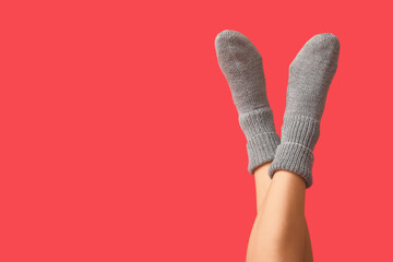 Legs of young woman in grey knitted socks on red background