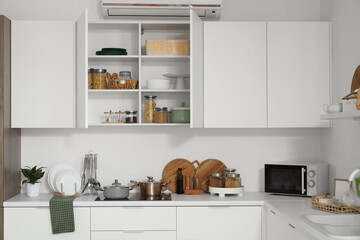 Open cupboard with utensils in light kitchen interior