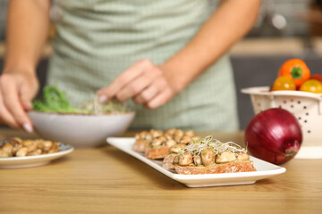 Tasty vegan bruschettas on table against woman cooking in kitchen, closeup