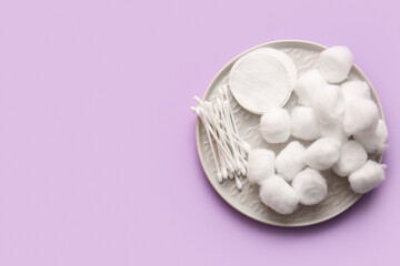 Plate with cotton balls, pads and swabs on lilac background