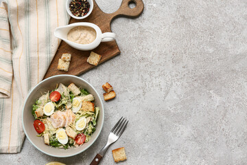 Bowl with tasty chicken Caesar salad, peppercorn and gravy boat of sauce on grey background