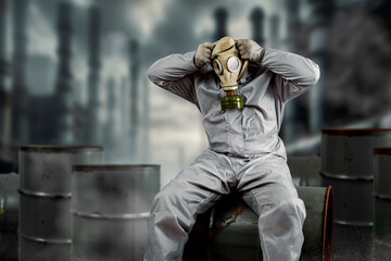 A man putting on or taking off gas mask dressed in protective suit sitting on a barrel of chemical...