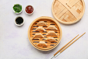 Fototapeta premium Bamboo steamer with tasty Japanese gyoza and bowls of sauces on white background