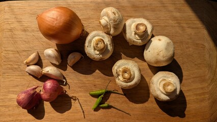 Raw ingredients on a chopping board in a sunny kitchen light, mushrooms, chilli, garlic, red onions...
