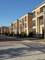 modern, multi-story residential buildings with large windows and beige stone facades. The architecture is elegant and contemporary. The weather is clear and sunny, with a bright blue sky