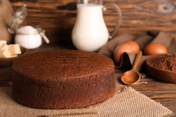 Tasty chocolate sponge cake with cocoa powder and eggs on wooden background