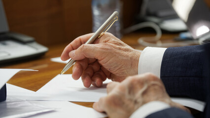 An elderly man's hand carefully signing a formal document with a sophisticated pen. Ideal for illustrating legal, political, or business negotiations and agreements. Photo