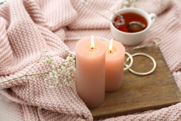 Burning candles, flowers and tray on knitted plaid near window