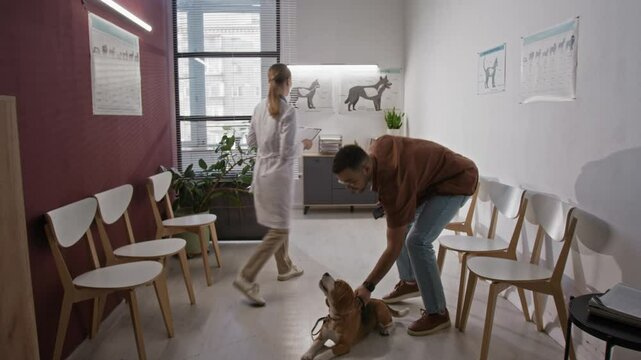 Female veterinarian inviting male dog owner to enter examination room for health checkup of beagle in clinic