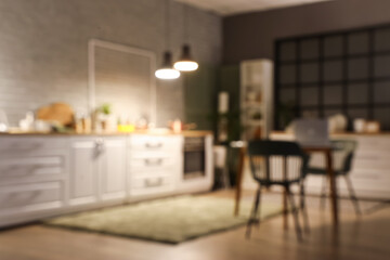 Blurred view of dark kitchen with counters, dining table and glowing lamps in evening