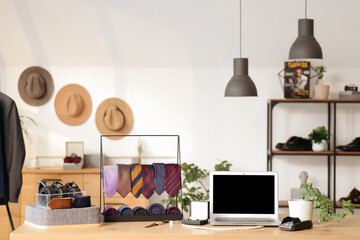 Stand with men's neckties and blank laptop on table in boutique