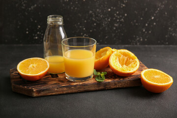 Glass and bottle of fresh orange juice with mint on black background