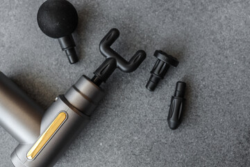 Modern massage gun with four interchangeable heads displayed on a grey textured surface, showcasing sleek design and multiple functionality options for muscle therapy